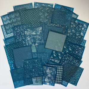 May include: A collection of 30 teal blue nail art stencils with white designs. The stencils feature a variety of patterns, including geometric shapes, floral designs, and abstract patterns.