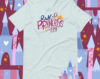May include: Light blue t-shirt with the text "Run Like a Princess 13.1" in pink and blue lettering with a gold crown and a heart. The shirt is surrounded by a pattern of pink and blue castles with gold stars.