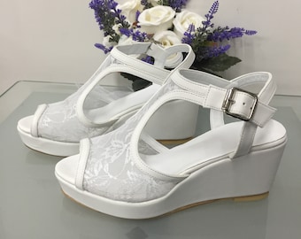 Può includere: Sandali con zeppa in pizzo bianco con chiusura a fibbia. I sandali hanno una suola platform e un design a T.