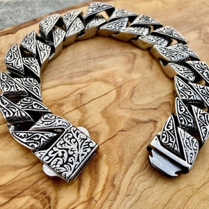 May include: A silver chain bracelet with a detailed floral pattern. The bracelet is made of metal and has a clasp closure.