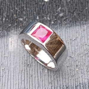 May include: A silver ring with a square-shaped, bright pink ruby gemstone set in the centre.