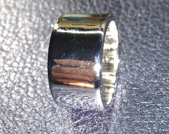 May include: A wide, polished silver-tone band ring with a smooth, reflective surface. The metal has a high-shine finish that captures light, creating bright highlights and dark shadows across the curved exterior of the circular jewelry piece.