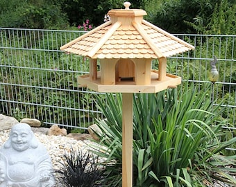 Könnte beinhalten: Ein Vogelhaus aus Holz mit einem Schindeldach und einem dreieckigen Sockel. Das Vogelhaus ist auf einer hohen Holzstange montiert.
