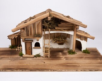 May include: A wooden nativity scene with a small, rustic barn with a whitewashed exterior. The barn has a ladder, a hayloft, and a stable door. The scene is set on a wooden base.