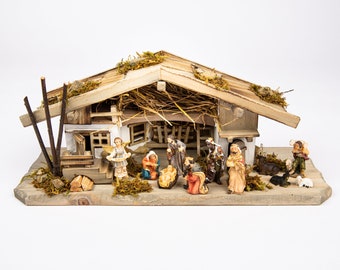 Puede incluir: Un belén de madera con un pequeño establo rústico y una colección de figuras que representan el nacimiento de Jesús. Las figuras incluyen a María, José, el niño Jesús, un ángel, pastores y animales.