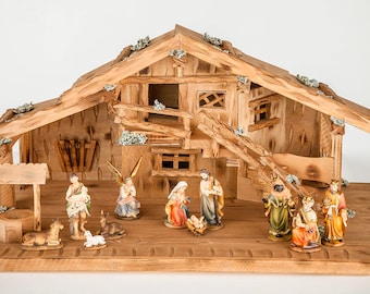 Puede incluir: Un belén de madera con un establo rústico detallado y una colección de figuras pintadas que representan la historia tradicional de Navidad. Las figuras incluyen a María, José, el niño Jesús, ángeles, pastores y magos.