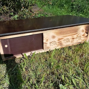 Peut inclure: Une maison en bois pour tortues avec un toit noir et une porte à charnières. La maison a trois silhouettes de tortues brûlées dans le bois.