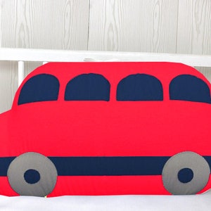 May include: A red bus-shaped pillow with blue windows and gray wheels. The pillow is made of soft fabric and is perfect for a child's room.