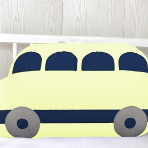 May include: A yellow bus-shaped pillow with blue windows and wheels. The pillow is in a white crib.