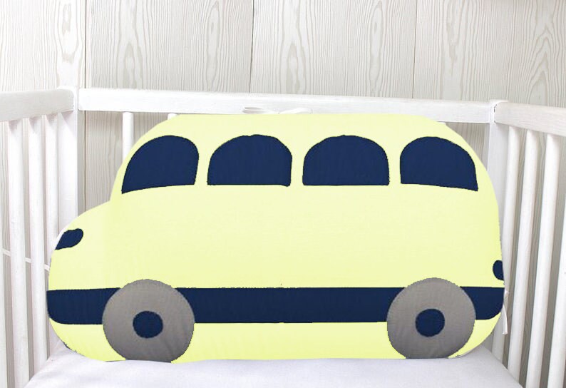 May include: A yellow bus-shaped pillow with blue windows and wheels. The pillow is in a white crib.