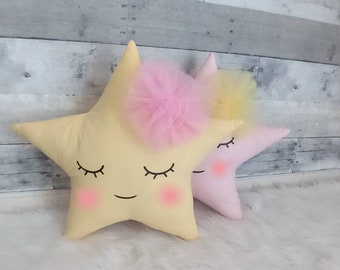 May include: Two plush star-shaped pillows with embroidered eyes and smiles. One pillow is yellow with a pink tulle bow and the other is pink.