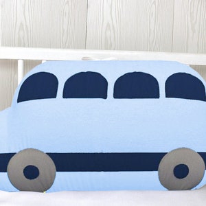 May include: A light blue bus-shaped pillow with dark blue windows and wheels. The pillow is in a white crib.