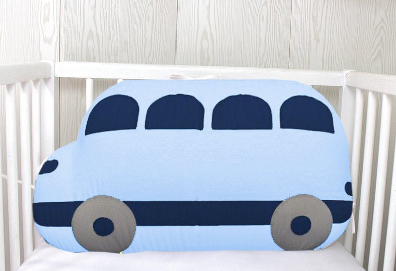May include: A light blue bus-shaped pillow with dark blue windows and wheels. The pillow is in a white crib.