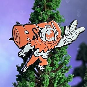 May include: Orange and white enamel pin of a cartoon astronaut wearing a helmet and a jetpack. The astronaut is flying with one arm raised in a rock and roll hand gesture.