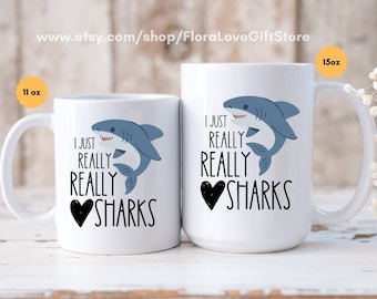 May include: Two white ceramic mugs with black text and a cartoon shark graphic. The text on the mugs reads "I just really really love sharks". The mug on the left is 11 oz and the mug on the right is 15 oz.