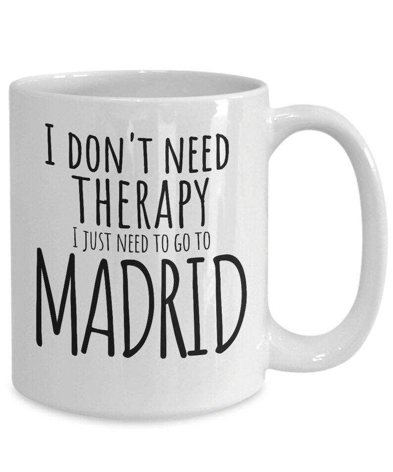 K&ouml;nnte beinhalten: Wei&szlig;e Keramik-Kaffeetasse mit schwarzem Text, der "Ich brauche keine Therapie, ich muss nur nach Madrid" lautet.