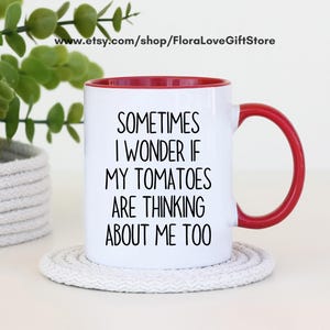 May include: White ceramic mug with a red interior and handle. The mug features the text "SOMETIMES I WONDER IF MY TOMATOES ARE THINKING ABOUT ME TOO" in black lettering. The mug is sitting on a white coaster.