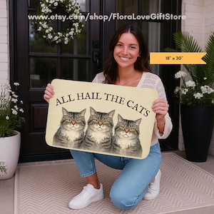 Könnte beinhalten: Eine rechteckige Fußmatte mit dem Text "ALL HAIL THE CATS" und drei Katzenporträts. Die Matte ist 46 cm x 76 cm groß und hat einen beigen Hintergrund. Die Katzen sind grau und braun getigert mit grünen Augen.