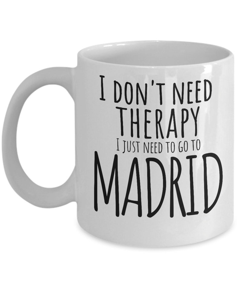 K&ouml;nnte beinhalten: Wei&szlig;e Keramik-Kaffeetasse mit schwarzem Text, der "Ich brauche keine Therapie, ich muss nur nach Madrid" lautet.