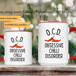 Può includere: Due tazze in ceramica bianca con bordi rossi. Entrambe le tazze presentano una grafica di peperoncino rosso e il testo "O.C.D. OBSESSIVE CHILLI DISORDER". La tazza più piccola è da 11 once e la tazza più grande è da 15 once.