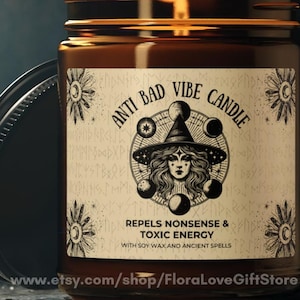 May include: A brown glass candle jar with a black lid, displaying a label that reads "ANTI BAD VIBE CANDLE". The label features a witch illustration and the words "REPELS NONSENSE & TOXIC ENERGY". The candle is made with soy wax and ancient spells.