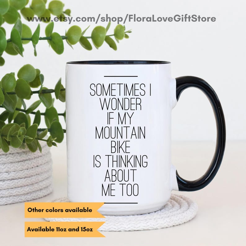 May include: White ceramic mug with a black handle and rim. The mug has black text that reads "Sometimes I wonder if my mountain bike is thinking about me too".