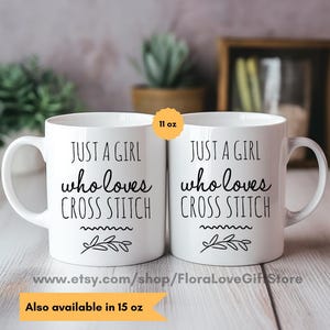 May include: Two white ceramic mugs with black text that reads "Just a girl who loves cross stitch" and a small floral design. The mugs are 11 ounces and are available in 15 ounces.