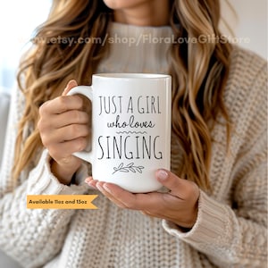 Op de afbeelding: Een witte keramische mok met een zwart ontwerp met de tekst "Just a girl who loves singing" met een klein blaadjesontwerp. De mok is verkrijgbaar in 11oz en 15oz.