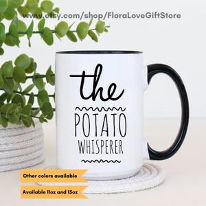 Puede incluir: Taza de cerámica blanca con asa y borde negros. La taza tiene texto negro que dice "the potato whisperer" con una línea ondulada arriba y abajo del texto.