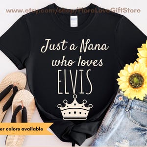 May include: Black t-shirt with the text "Just a Nana who loves ELVIS" in white script, a crown graphic, and the words "Other colors available" on a banner. The shirt is paired with blue jeans, flip-flops, and sunflowers.