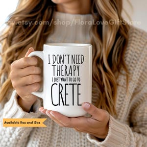 Op de afbeelding: Een witte keramische mok met een handvat, voorzien van de zwarte tekst: I DON'T NEED THERAPY I JUST WANT TO GO TO CRETE. De mok is verkrijgbaar in de maten 325 ml en 444 ml, zoals aangegeven in de tekst linksonder in de afbeelding.