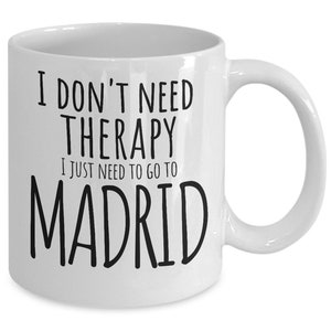 K&ouml;nnte beinhalten: Wei&szlig;e Keramik-Kaffeetasse mit schwarzem Text, der "Ich brauche keine Therapie, ich muss nur nach Madrid" lautet.