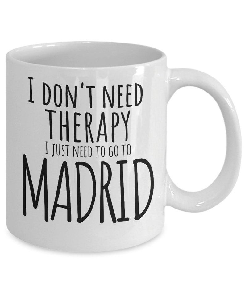 K&ouml;nnte beinhalten: Wei&szlig;e Keramik-Kaffeetasse mit schwarzem Text, der "Ich brauche keine Therapie, ich muss nur nach Madrid" lautet.