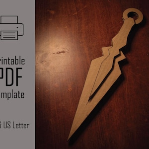 Puede incluir: Una plantilla de kunai de papel marrón con un anillo en el extremo del mango, sobre una superficie de madera oscura. La imagen incluye el texto "Printable PDF Template" y "A4 & US Letter".
