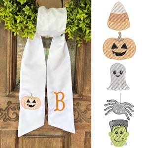 May include: White Halloween-themed door hanger with a pumpkin and the letter "B" embroidered in orange. The hanger is adorned with a green wreath. Additional embroidered Halloween designs include candy corn, a jack-o'-lantern, a ghost, a spider, and Frankenstein's monster.