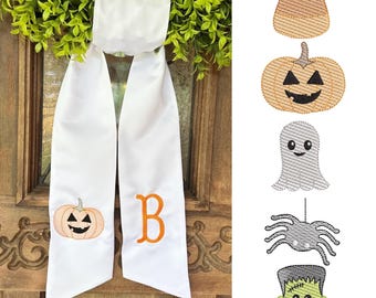 May include: White Halloween-themed door hanger with a pumpkin and the letter "B" embroidered in orange. The hanger is adorned with a green wreath. Additional embroidered Halloween designs include candy corn, a jack-o'-lantern, a ghost, a spider, and Frankenstein's monster.