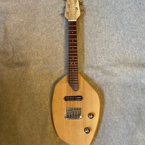 May include: A custom-made, light-colored wooden electric guitar with a unique, asymmetrical body shape. The guitar features a fretboard, tuning pegs, and chrome hardware, including a bridge and two control knobs. The instrument is designed for playing music.