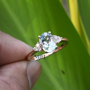 May include: A rose gold ring with a light blue oval aquamarine gemstone and three smaller round diamonds. The ring is set in a delicate prong setting.