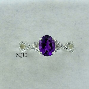 May include: A silver ring featuring a large oval amethyst gemstone, surrounded by smaller clear gemstones. The ring has a twisted band.