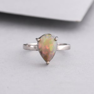 May include: A pear-shaped opal ring set in silver. The opal is a milky white with flashes of green and yellow.