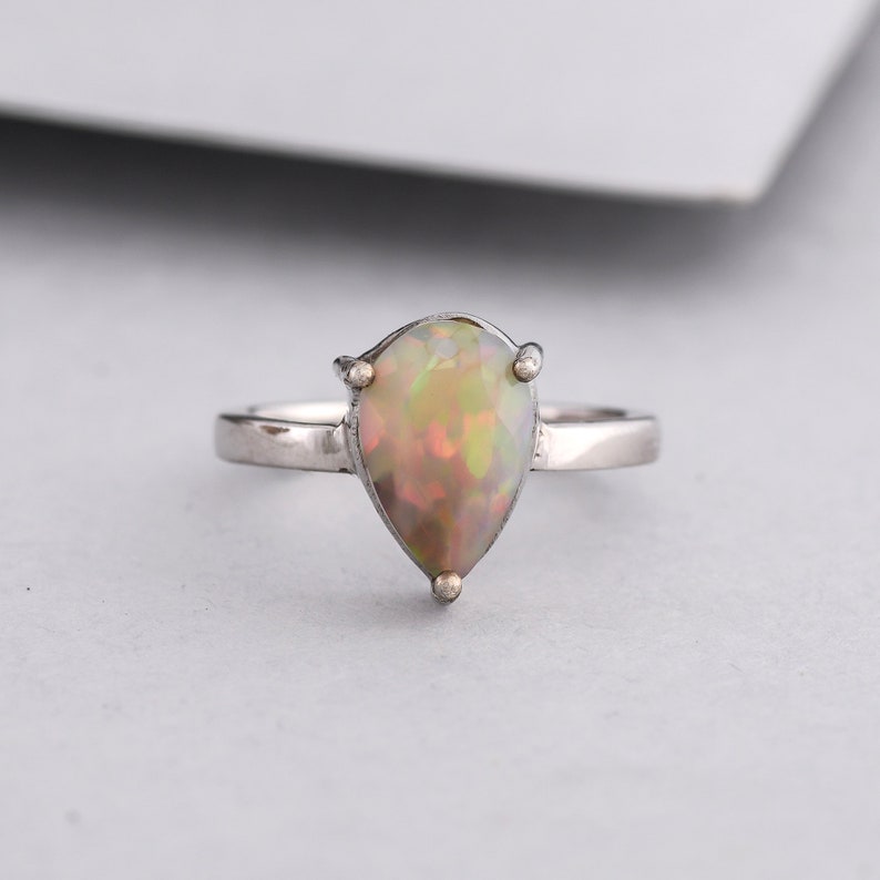 May include: A pear-shaped opal ring set in silver. The opal is a milky white with flashes of green and yellow.