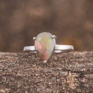 May include: A pear-shaped opal ring set in silver. The opal is a milky white with flashes of green, blue, and orange.