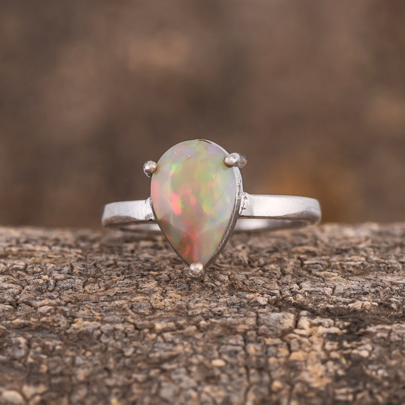 May include: A pear-shaped opal ring set in silver. The opal is a milky white with flashes of green, blue, and orange.