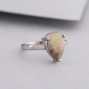 May include: A silver ring with a pear-shaped opal gemstone. The opal has a rainbow of colors, including green, yellow, and pink.