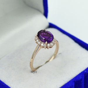 May include: A gold ring with a large oval purple gemstone surrounded by a halo of smaller white gemstones.