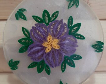 Puede incluir: Una flor de papel morada y amarilla con hojas verdes sobre un fondo blanco. La flor está hecha de papel y tiene un diseño delicado e intrincado.