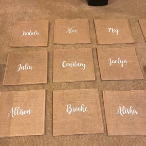 May include: Ten brown burlap placemats with white lettering. The names on the placemats are:  Isabella, Alex, Meg, Julia, Courtney, Jaclyn, Allison, Brooke, Alisha.