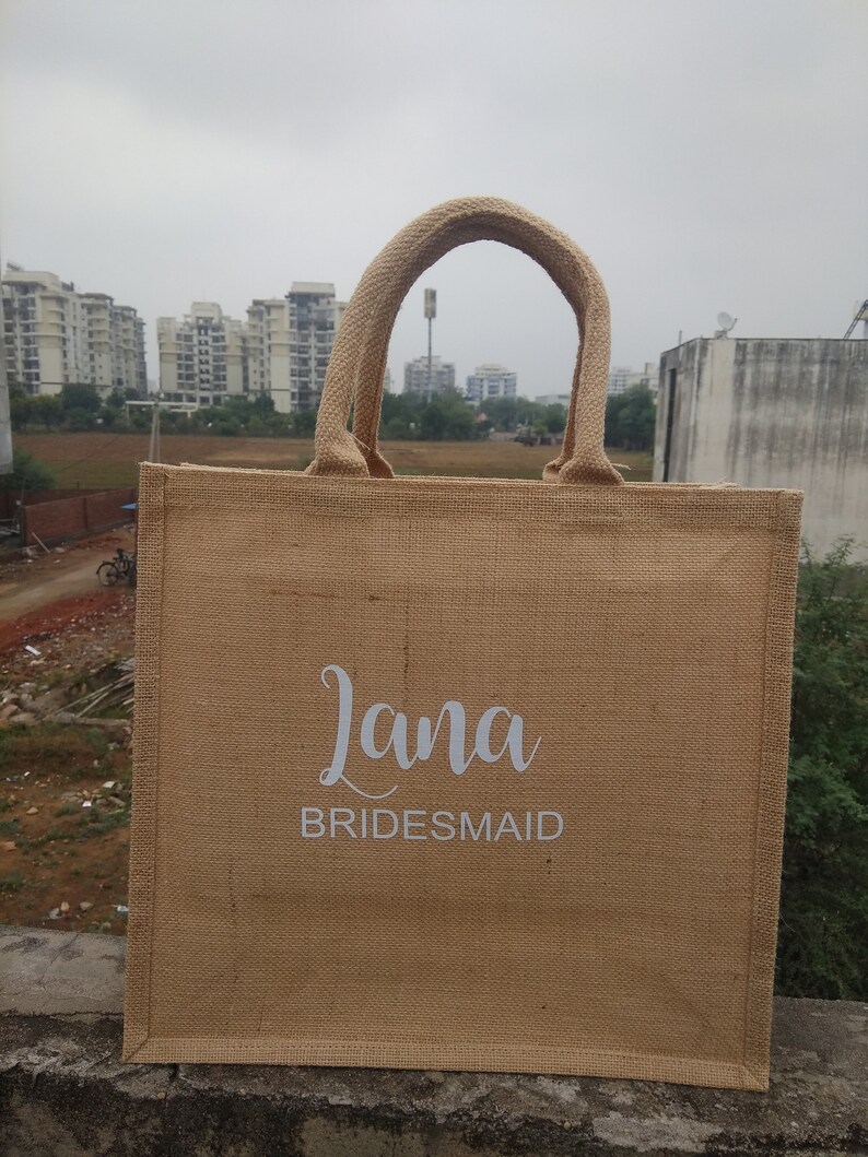 May include: A brown burlap tote bag with white handles and the text "Lana Bridesmaid" printed on the front.