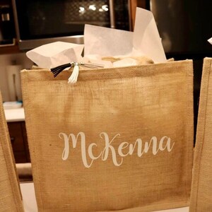 May include: A brown burlap tote bag with a white tassel and the name "McKenna" printed on the front.