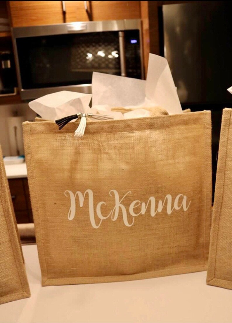 May include: A brown burlap tote bag with a white tassel and the name "McKenna" printed on the front.